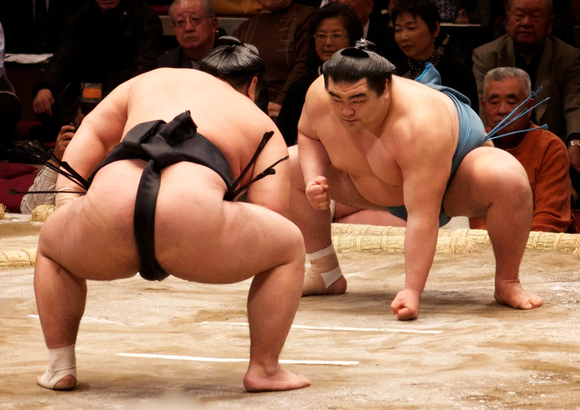 Two sumo wrestlers in mid-clash on the raised clay dohyo ring during a grand tournament bout
