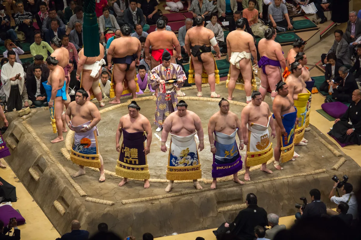 Sumo wrestlers in ornate ceremonial kesho-mawashi aprons perform the ring-entering ceremony around the dohyo