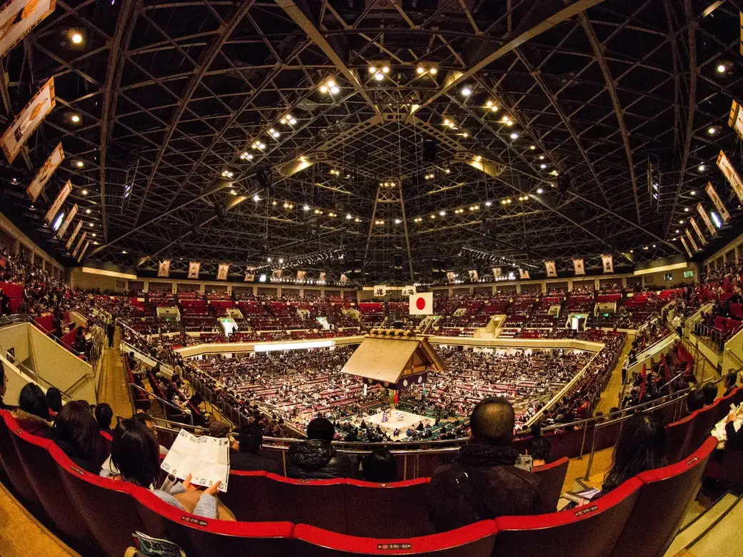 The packed interior of the Ryogoku Kokugikan sumo arena in Tokyo with the shrine-like roof suspended over the ring